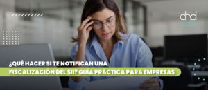 Mujer preocupada revisando documentos ante una laptop, simbolizando una empresa recibiendo una fiscalización del SII. Logo AHD Auditores.